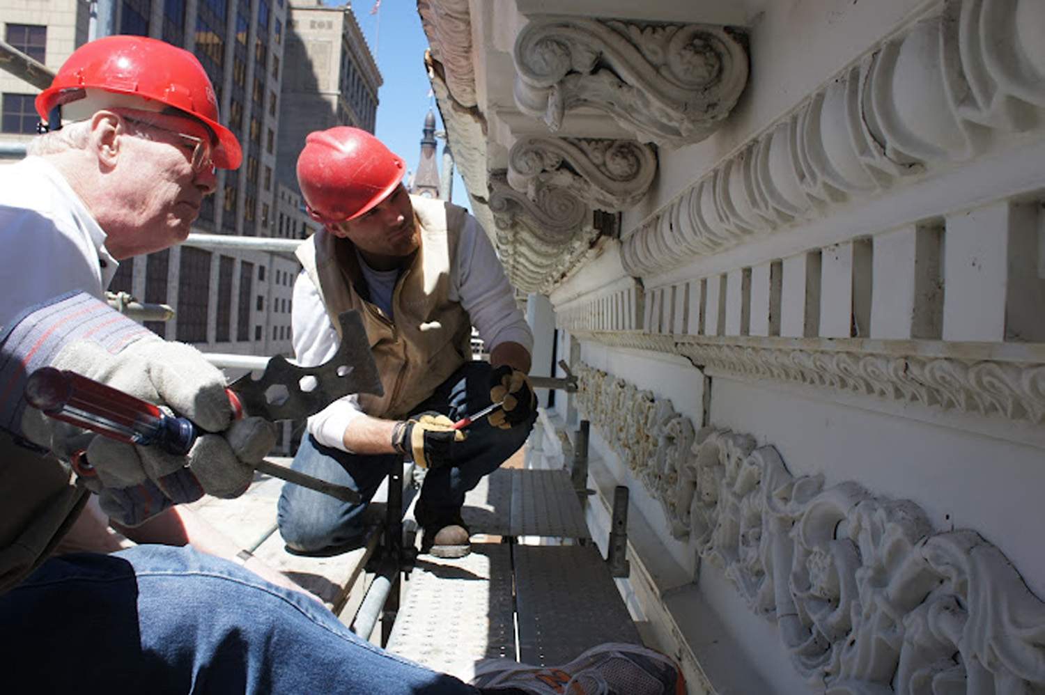 Iron Block building restoration - workers compare cast iron cornice to sheet metal cornice